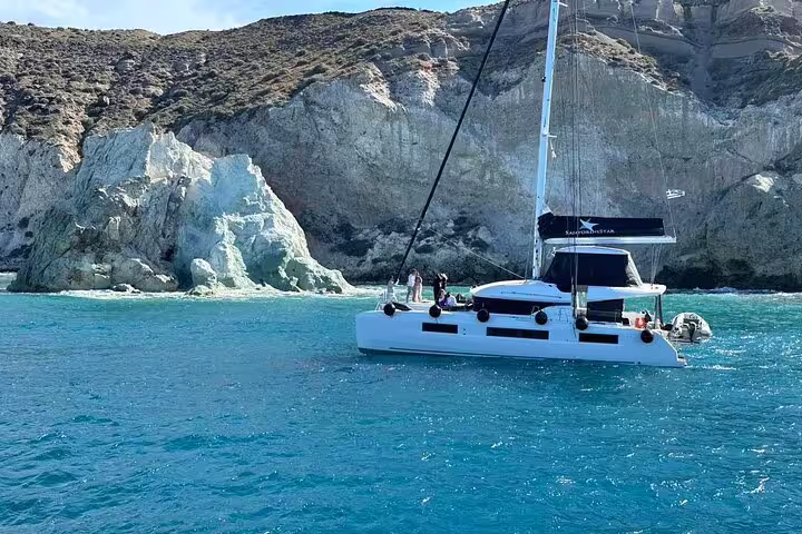 Luxurious catamaran sails near rocky cliffs on a premium Santorini cruise tour.
