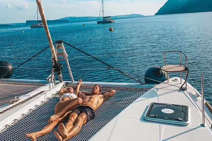 Relaxing on a catamaran deck during a half-day premium cruise in Santorini with views of Oia and the Aegean Sea.