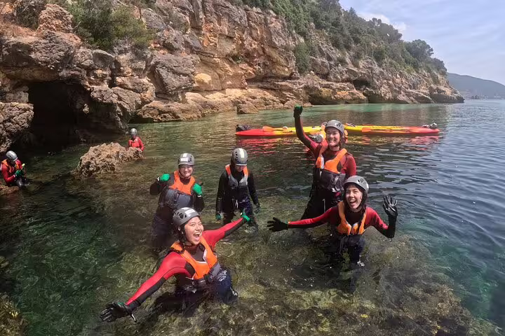 Group of excited adventurers in wetsuits and helmets enjoying coasteering in clear waters near Lisbon.