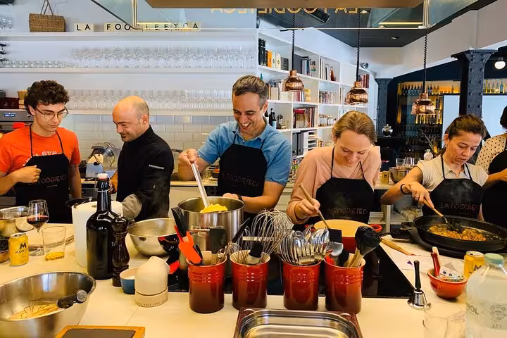 Group of people cooking paella in a designer loft during a premium Spanish cooking class, showcasing culinary skills.
