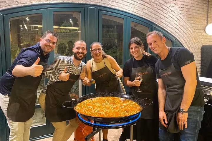 Group of people in aprons happily cooking paella in a stylish Spanish loft during a premium cooking class.
