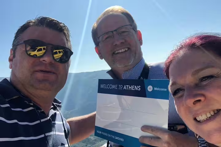 Guests on a private Athens day tour holding “Welcome to Athens” sign with mountain viewpoint backdrop