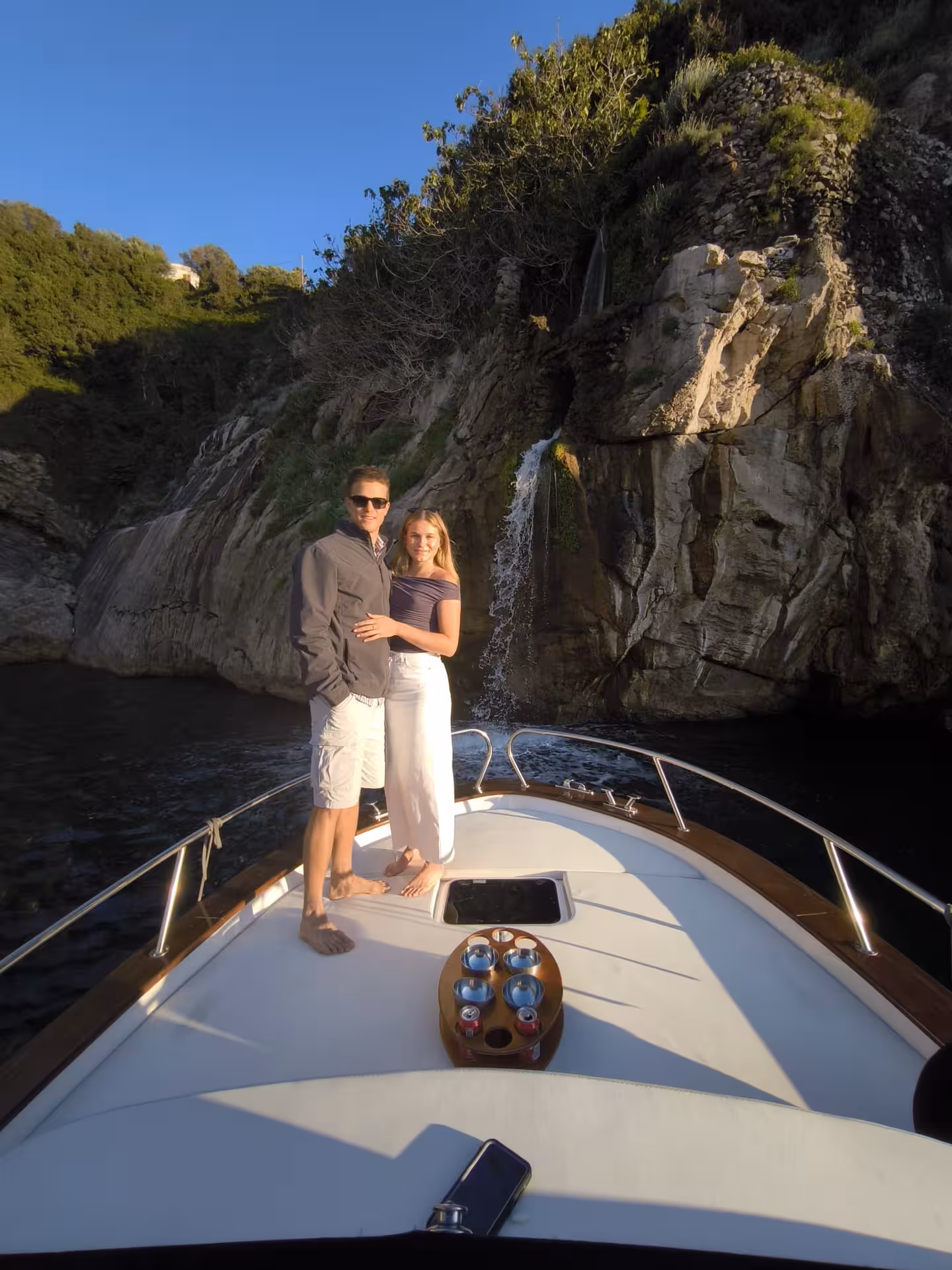 Couple enjoying a romantic moment on a private boat in Capri, with a scenic waterfall and rocky backdrop.
