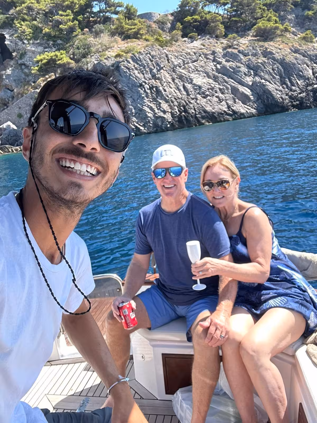 Happy tourists enjoying drinks on a private boat tour with scenic rocky cliffs near Capri.