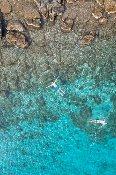 Aerial view of swimmers in crystal-clear turquoise Adriatic cove, perfect stop on a private boat tour Croatia