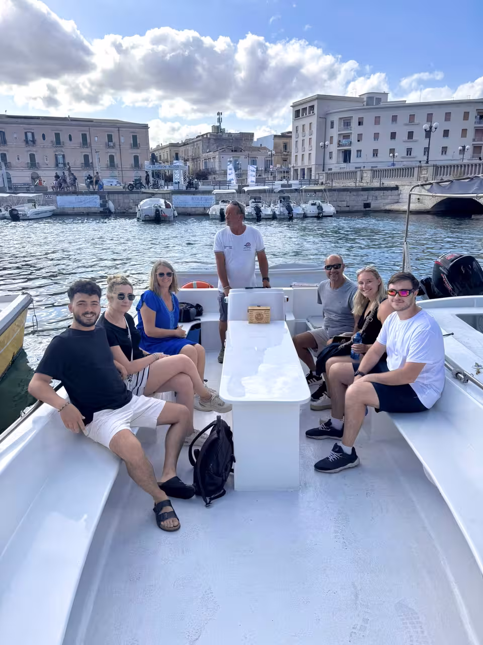 Group enjoying a private boat tour with city skyline and moored boats in the picturesque harbor.