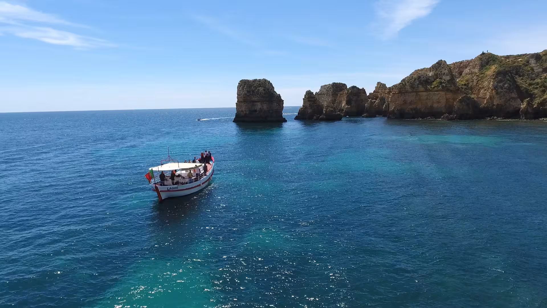 Boat cruising past Ponta da Piedade sea stacks near Lagos on Algarve sunset cruise over clear blue water