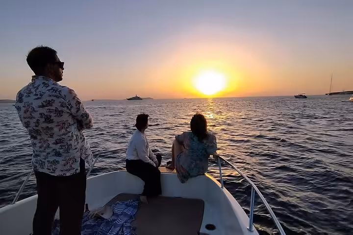 Group enjoying a stunning sunset on a private boat tour in San Antonio, perfect for paddle surfing and snorkeling.