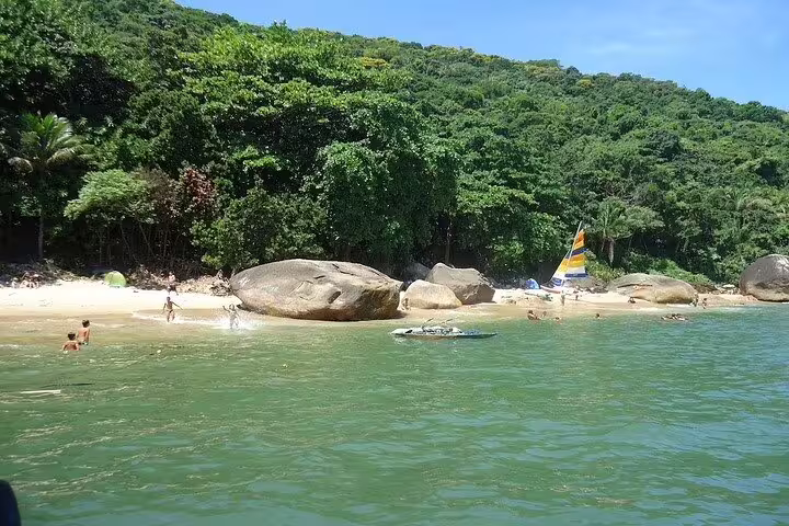 Idyllic beach with lush trees and rocks, a scenic stop on the full-day private boat tour in Santos with barbecue.