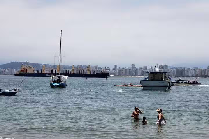 Families enjoying coastal waters with boats and a city skyline in view during a Santos beach outing.