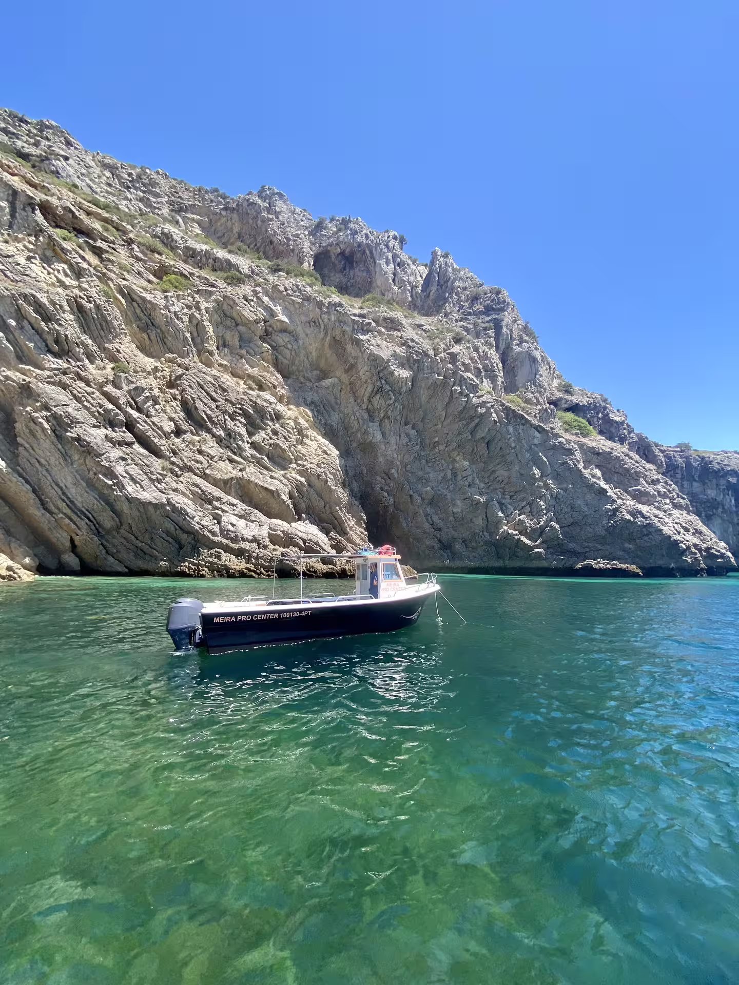 Private boat tour in Sesimbra's Arrábida Park with stunning clear turquoise waters and majestic rocky cliffs under a blue sky.