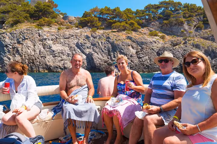 Group enjoys a relaxing meal on a Typical Gozzo boat surrounded by scenic cliffs on a Sorrento to Amalfi private tour.