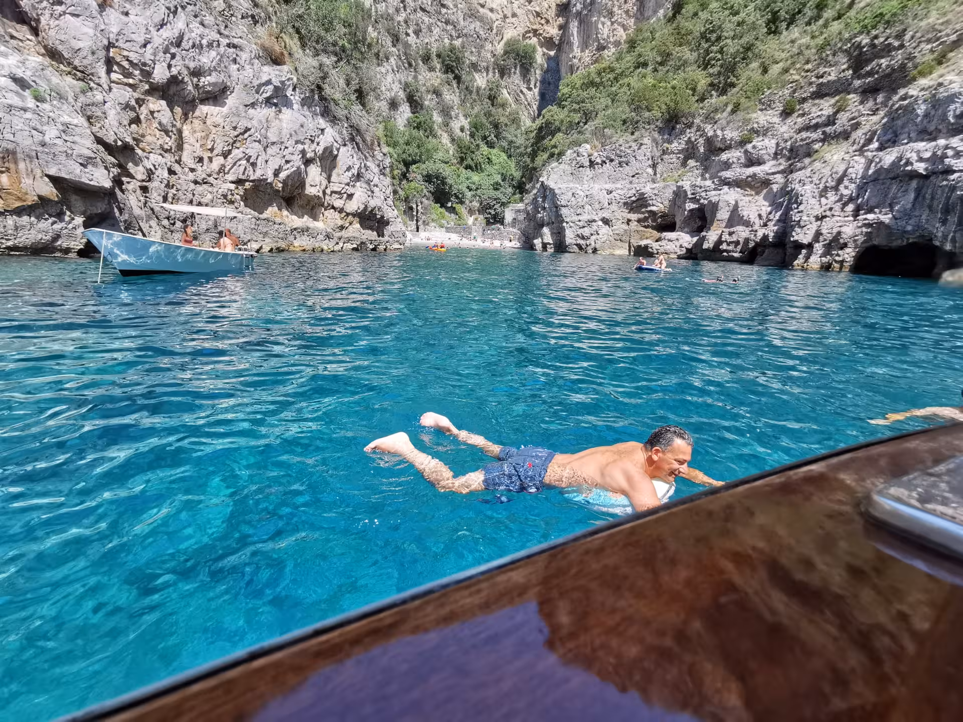 Man swimming in crystal-clear waters near rocky cliffs on a private boat tour from Sorrento to Amalfi.