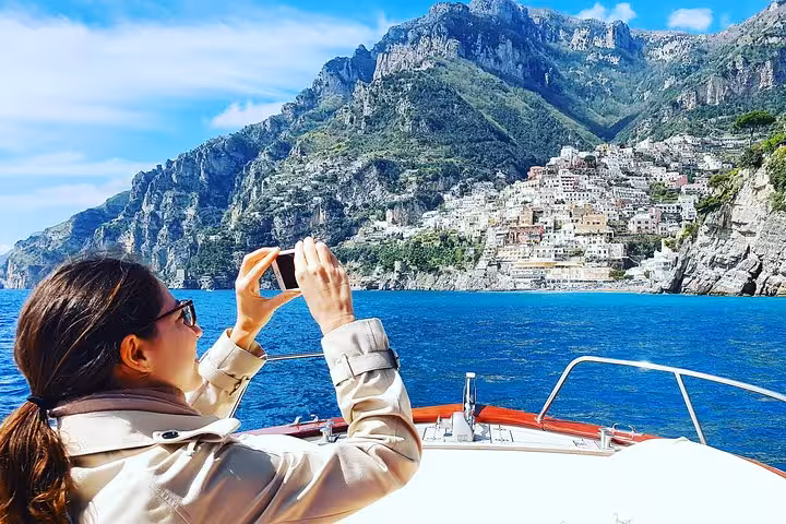 Woman captures stunning views of Positano from a Typical Gozzo boat during a private tour from Sorrento to Amalfi.