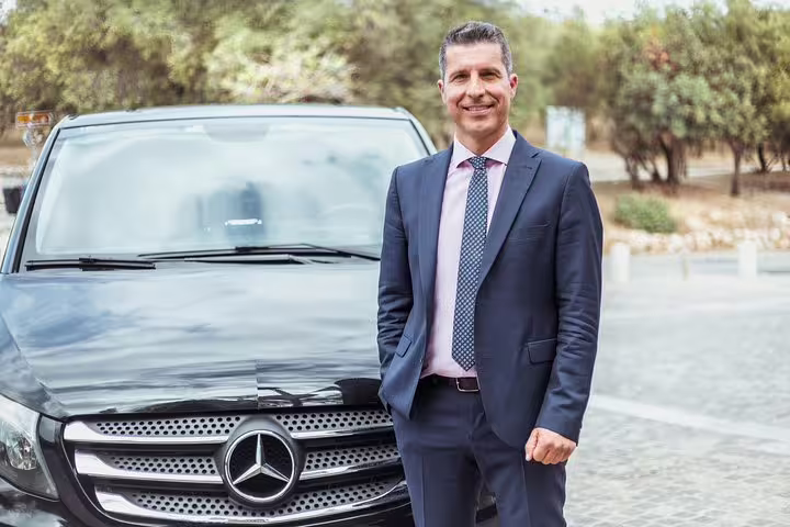 Friendly chauffeur standing beside a luxury Mercedes van, ready for a private day trip from Brussels to Bruges.