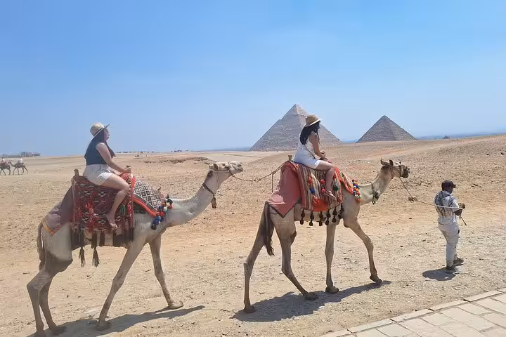 Tourists enjoy a camel ride with the majestic Pyramids of Giza in the background during a private Cairo highlights tour.
