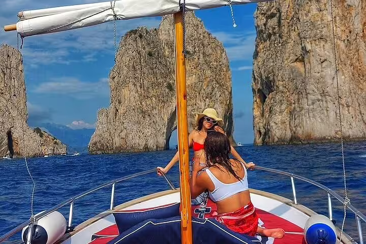 Private Capri boat tour passing the Faraglioni rocks, guests relaxing on deck during a 2-hour cruise