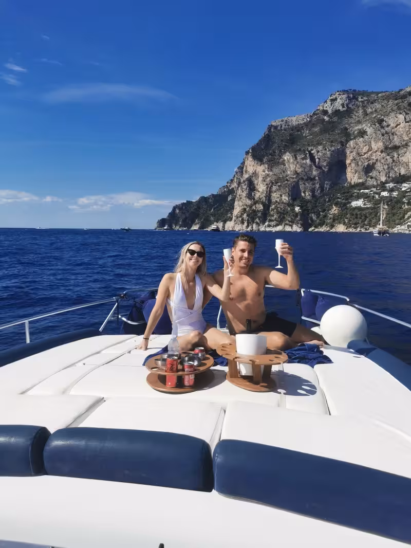 Couple enjoying drinks on a luxury boat during private Capri tour from Sorrento, with stunning cliff views.