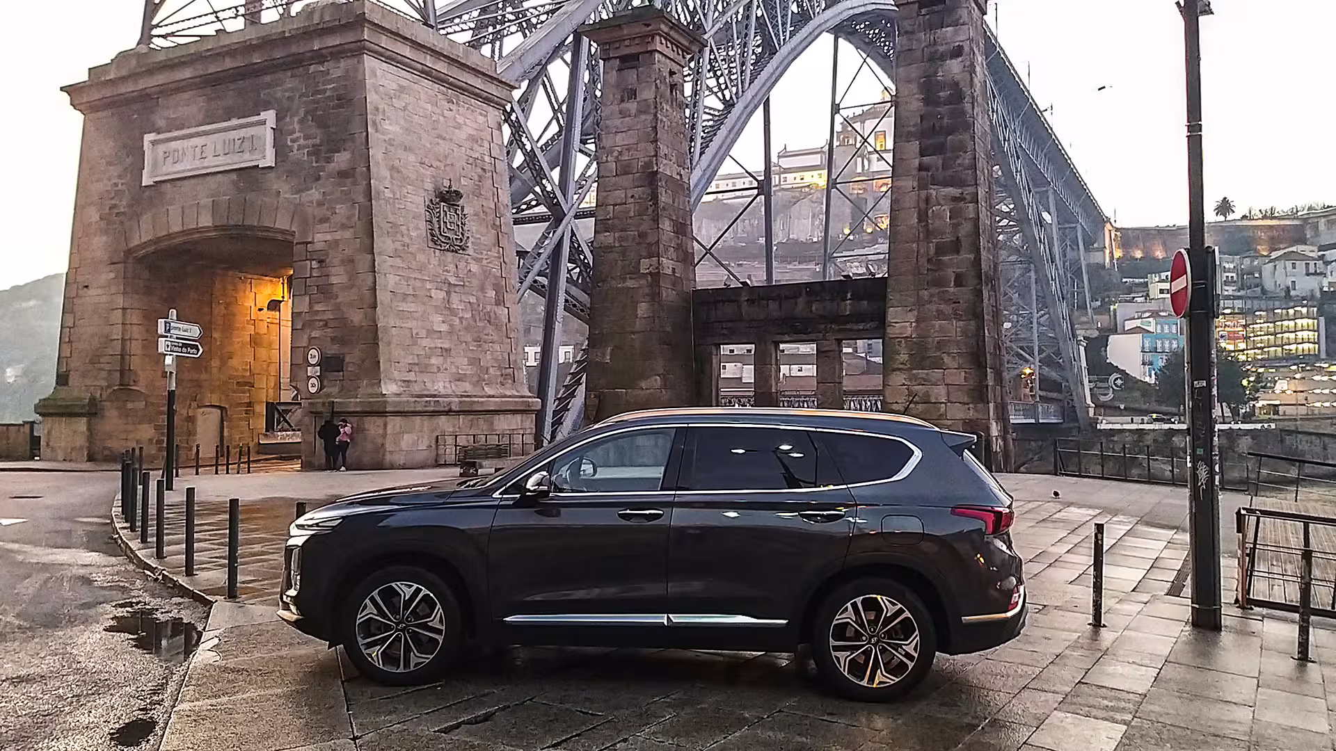 Private car transfer service with a luxury SUV parked by the iconic Ponte Luiz I bridge in Porto at dusk.