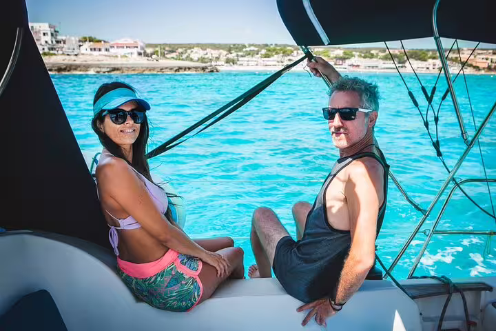 Couple enjoying a sunny day on a private catamaran in Ibiza, with turquoise waters and scenic coastline in the background.