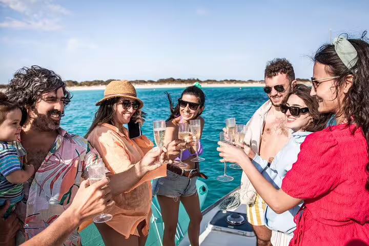 Group of friends enjoying a toast on a private catamaran in Ibiza's turquoise waters during a full-day Formentera trip.