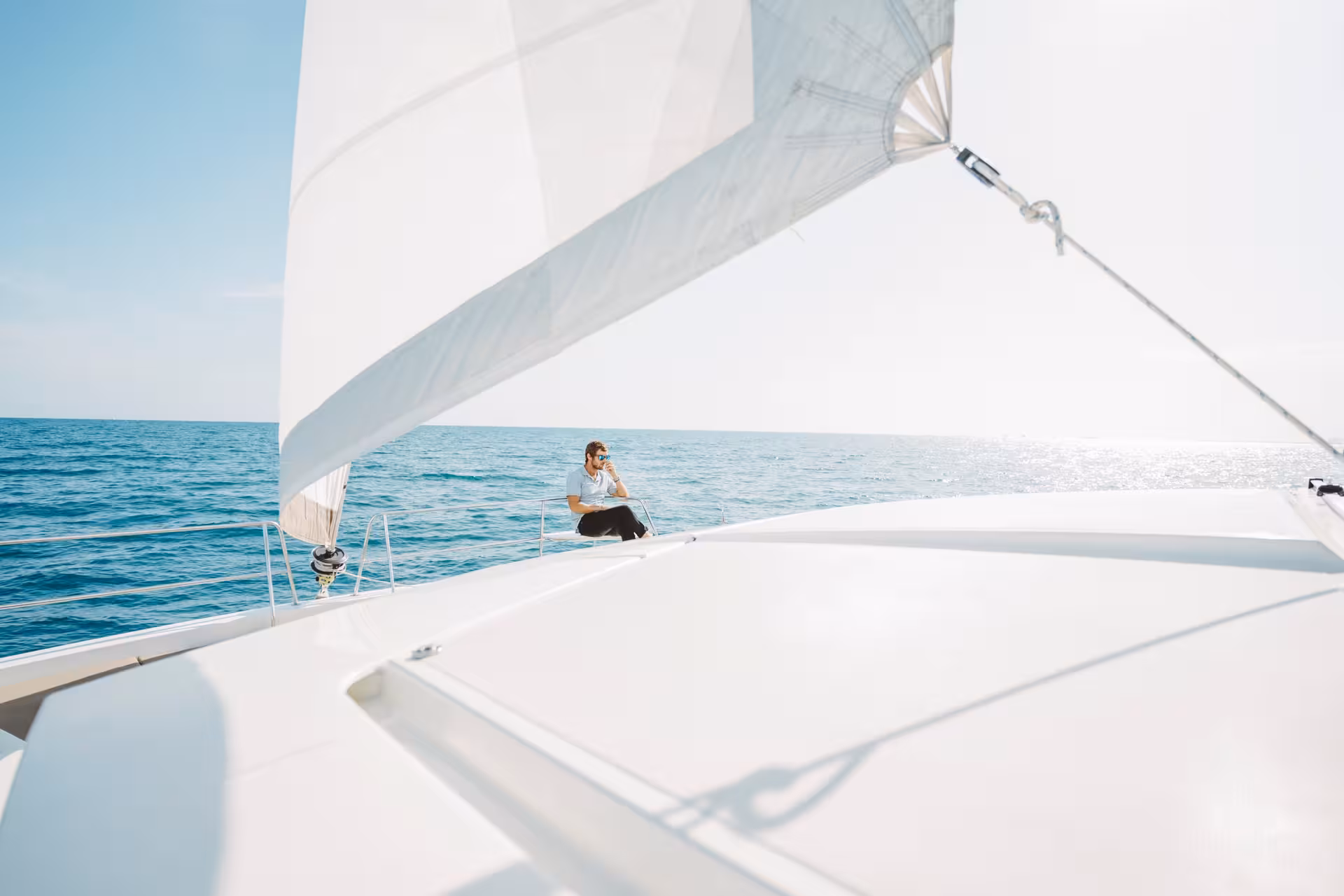Relaxing on a private catamaran rental under white sails, cruising calm blue sea on a sunny day