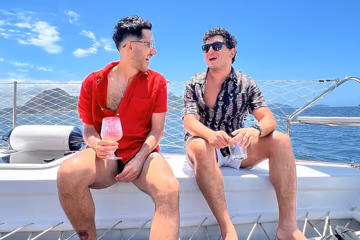 Friends relax on a private catamaran in Rio, enjoying open bar drinks on a 5-hour sailing tour