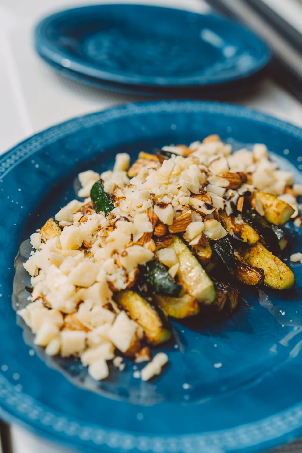 Private chef plated roasted zucchini with chopped almonds and crumbled cheese on a blue plate, gourmet dining