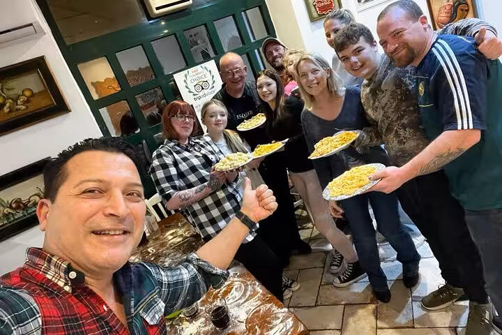 Group of happy participants holding plates of pasta at a private cooking class in Rome, capturing a fun culinary experience.