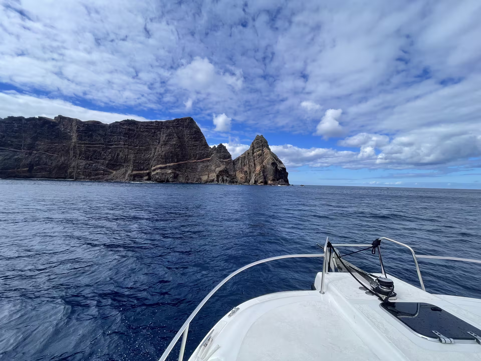 Private cruise boat approaching dramatic rocky cliffs under a vibrant blue sky, ideal for an afternoon tea experience.