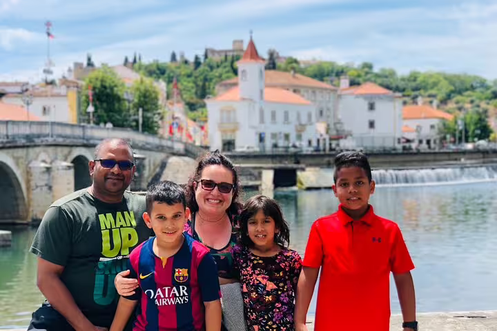Family enjoying a private day tour in Tomar by the scenic riverside, with historic Knights Templar architecture in the background.