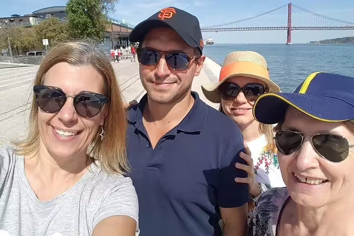 Group enjoying a customizable private day trip from Lisbon to Tomar, with scenic views of the 25 de Abril Bridge in the background.
