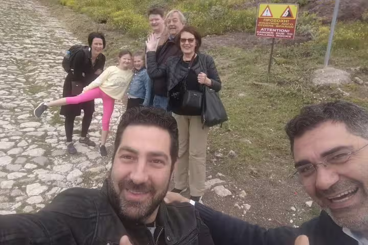 Group of tourists enjoying a private day trip from Athens to Delphi, posing on a scenic cobblestone path with greenery.