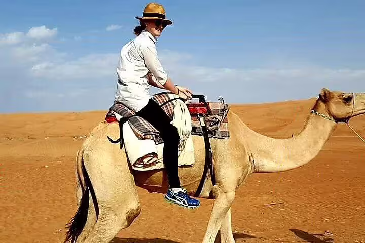Traveler enjoys camel ride under clear blue skies on private desert adventure trip.
