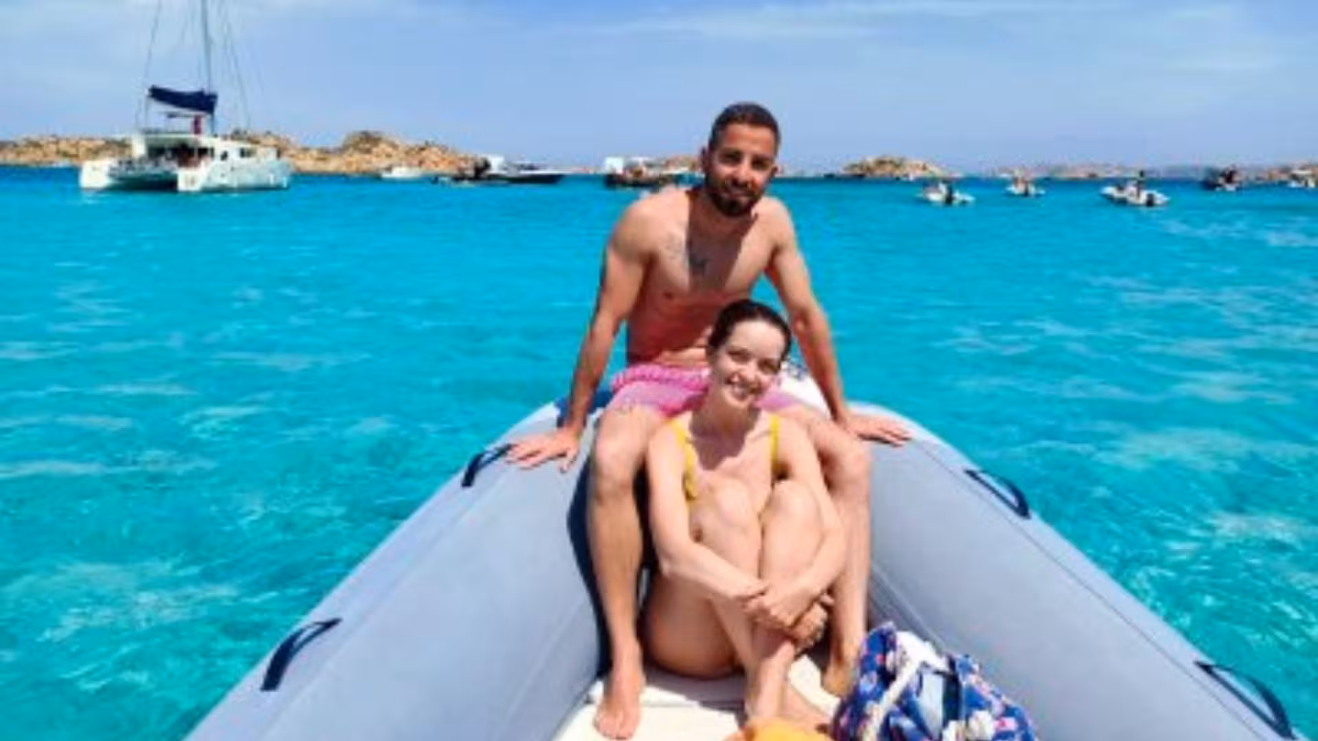 Couple enjoying a private dinghy tour on turquoise waters near La Maddalena, with scenic coastal views.