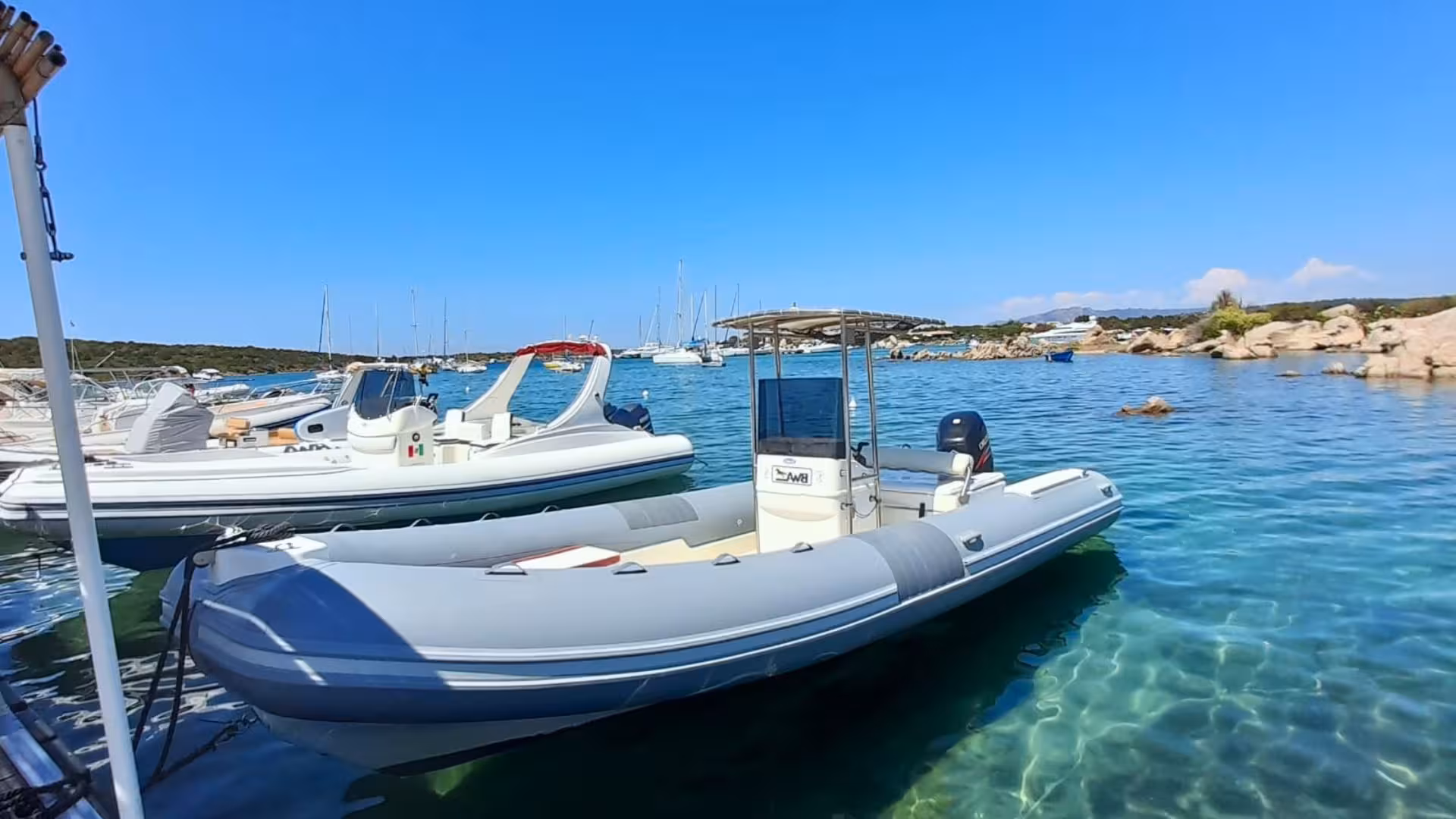 Private dinghy ready for a scenic tour between Tavolara and Porto Cervo with clear blue waters and moored boats.