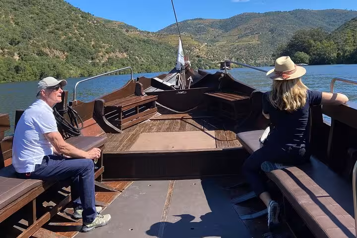Private Douro River boat cruise with guests relaxing on deck, scenic vineyards and hills on luxury tour