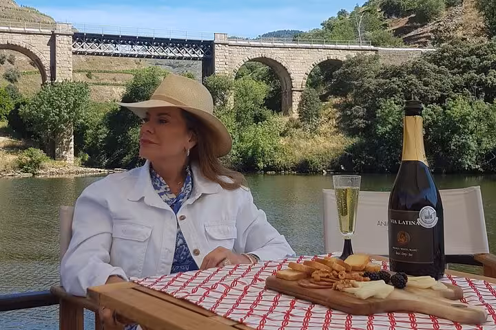 Private Douro boat tour picnic with sparkling wine and charcuterie by river bridge, luxury experience