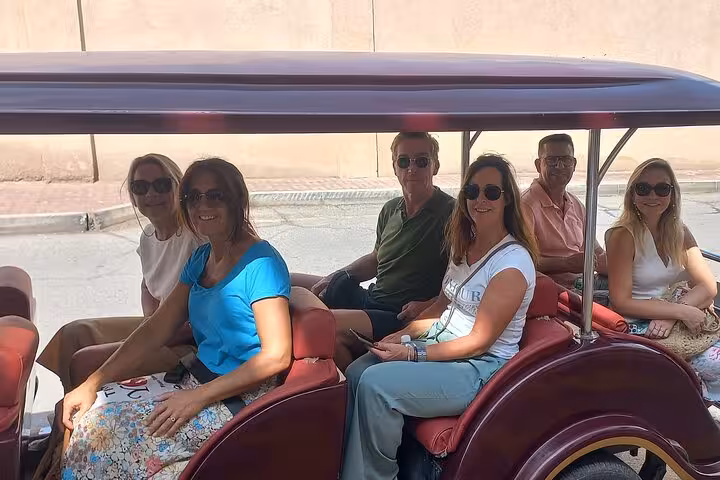 Small group of international travelers ride an open electric cart during a private evening sightseeing tour in historic Nizwa, Oman.