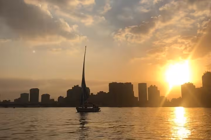 Private felucca cruise on the Nile River in Cairo during sunset, sailboat silhouette against skyline and sun