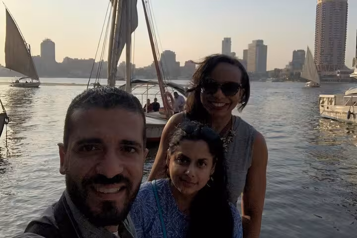 Guests smiling on a private felucca sailboat ride on the Nile River in Cairo with skyline at sunset