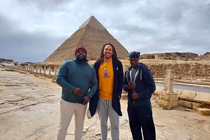 Visitors stand near the Giza Pyramid during a private tour featuring the Sphinx, Memphis, Saqqara, and a camel ride experience.