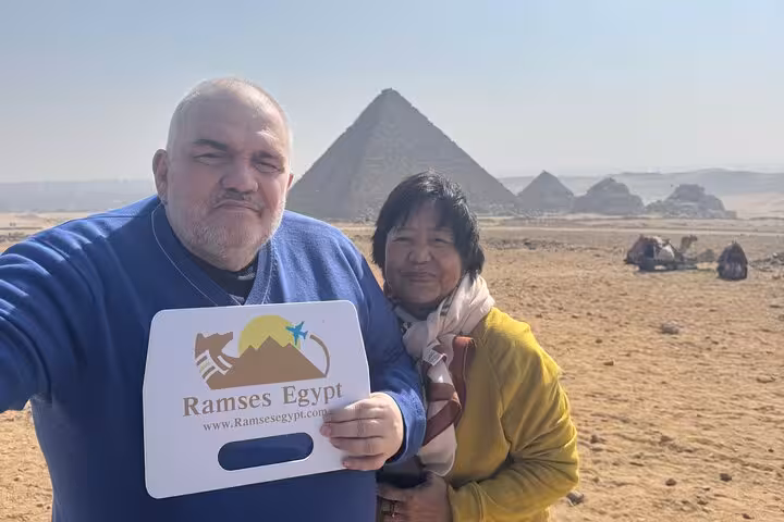 Private Giza Pyramids tour photo with travelers in desert, Great Pyramid behind, camel ride nearby Cairo