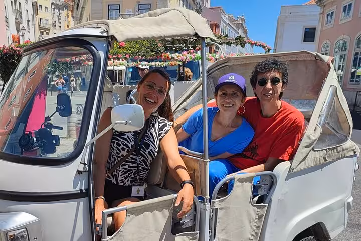 Happy travelers riding a tuk tuk on a 2-hour private historic Lisbon tour through downtown streets