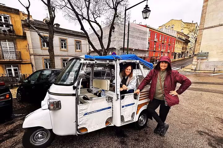 Guests pose beside a tuk tuk on a private historic Lisbon tour, exploring colorful old town streets