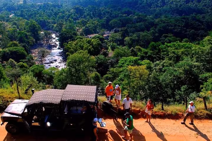 A group of tourists stands by a jeep, overlooking a scenic forest and river view on a Paraty private tour.