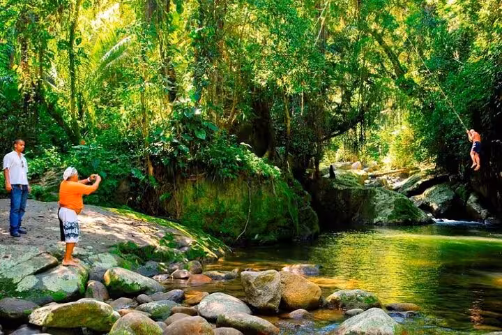 Tourists enjoy a lush jungle setting by a serene river in Paraty, perfect for a private jeep tour adventure.