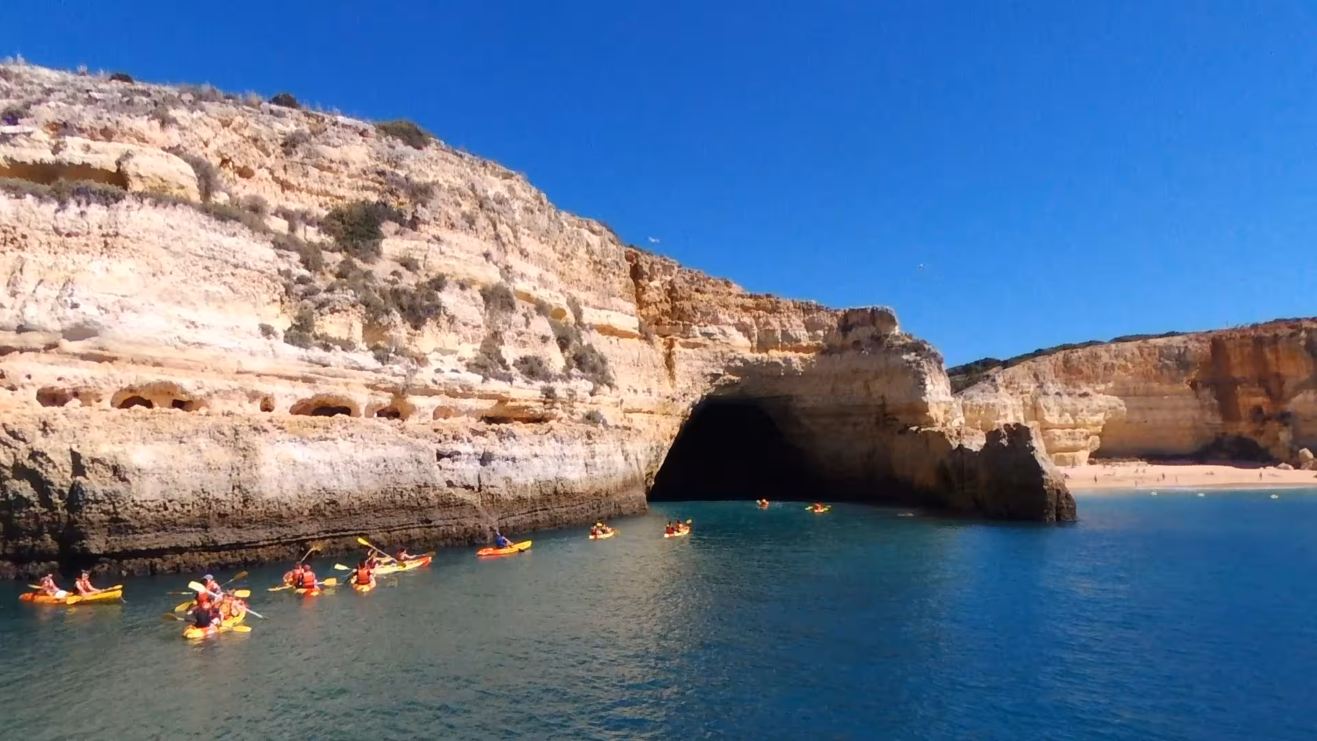 Group of kayakers paddling along Algarve cliffs toward a sea cave entrance on a guided private Benagil kayak tour