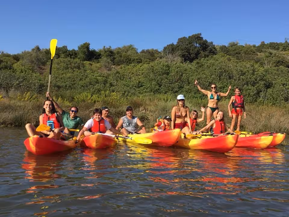 Smiling group paddling bright tandem kayaks on calm river with green banks, enjoying guided private kayak tour experience