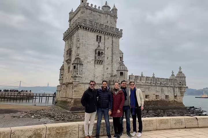 Group of tourists enjoying a private Lisbon city tour in front of the historic Belém Tower on a cloudy day, highlighting cultural exploration.